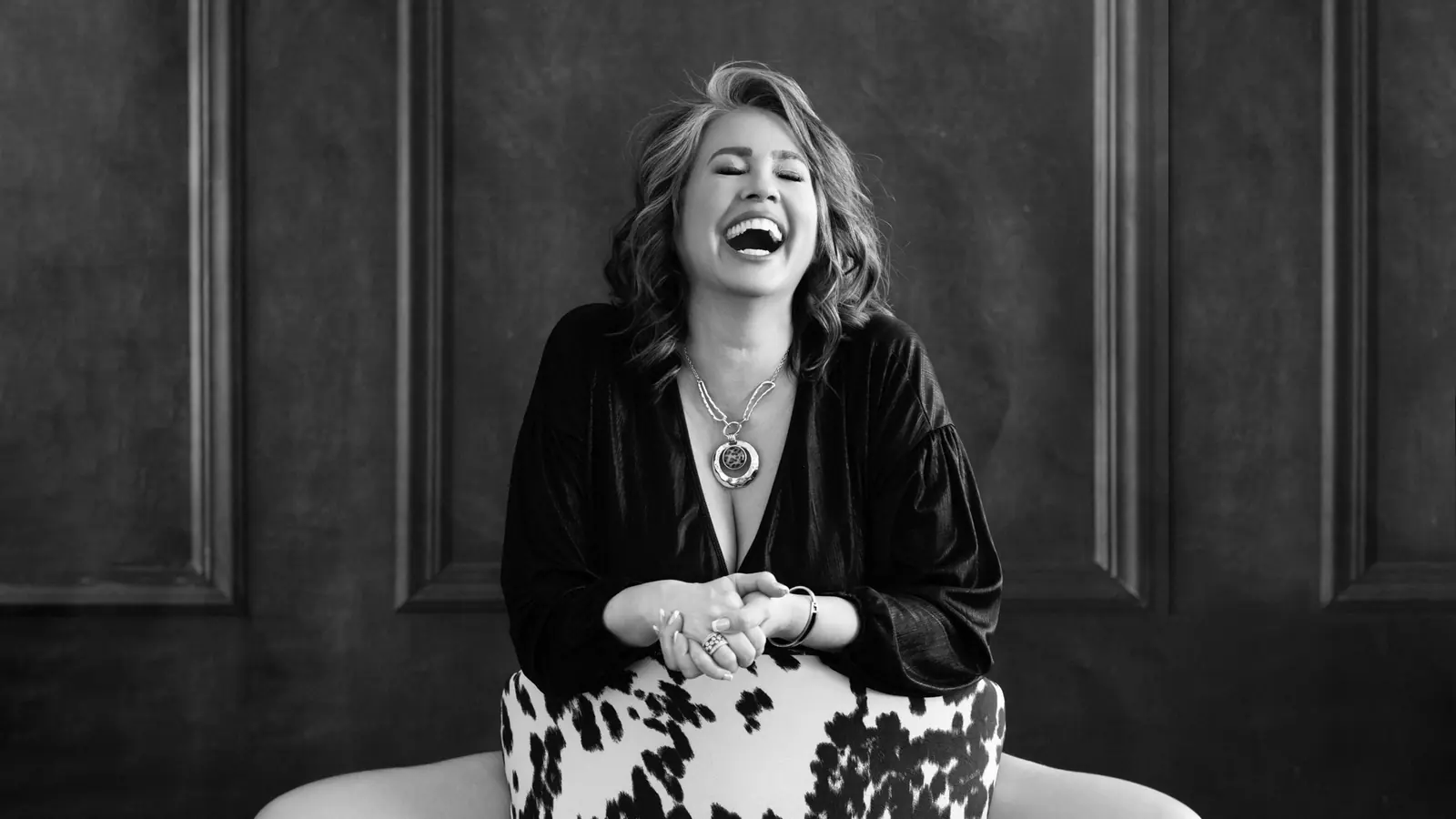 Black and white studio portrait of a woman over 50 laughing in a chair
