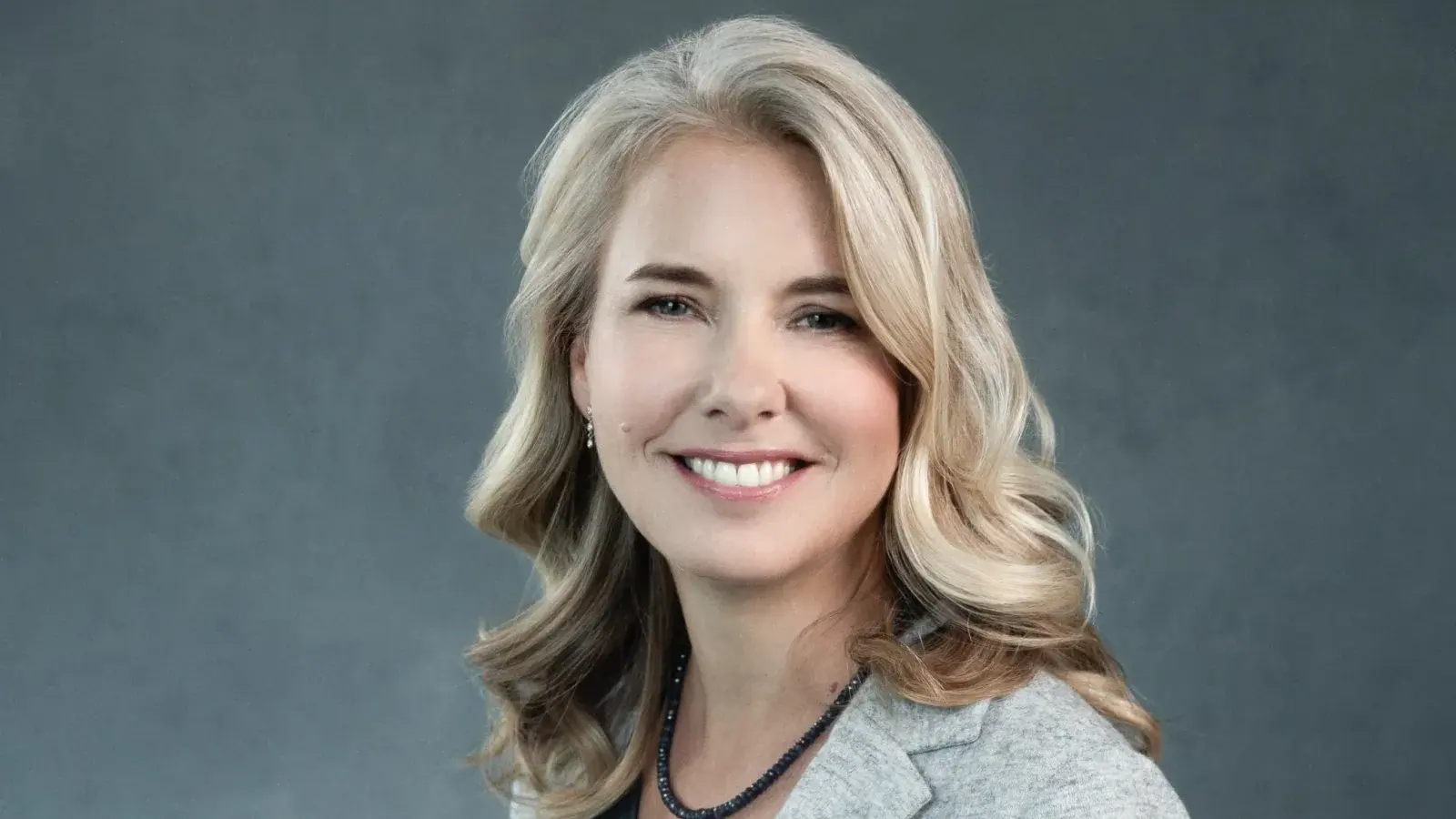 Tight studio headshot of a smiling woman against a soft gray backdrop, photographed in Charlottesville