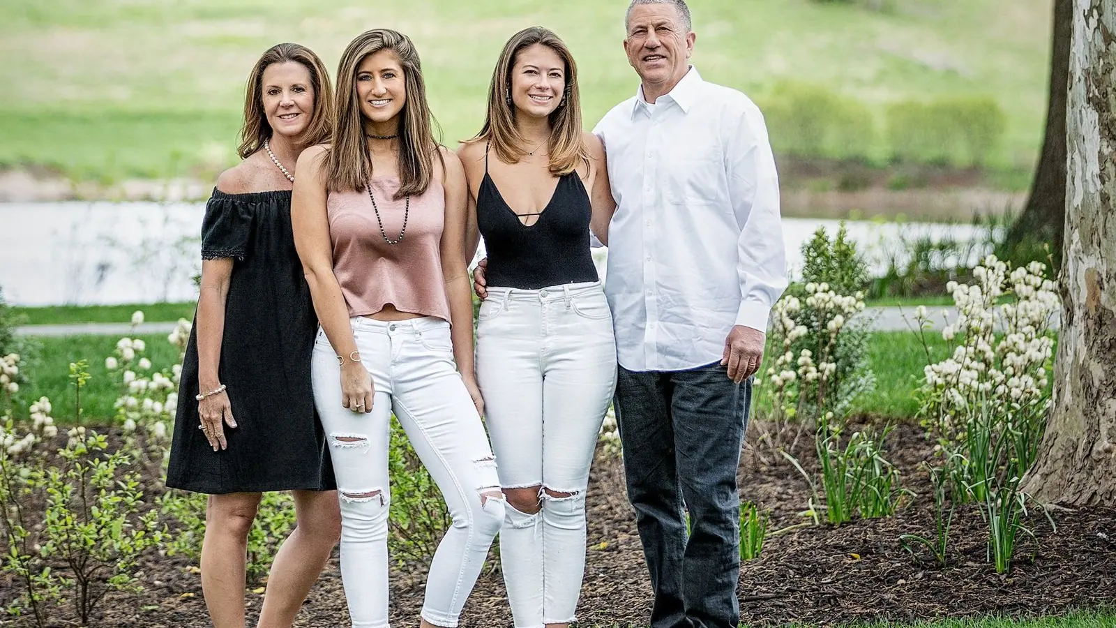 Family of four in coordinated black, white and blush outfits standing close together in a spring garden