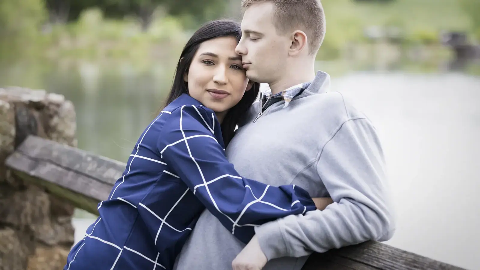 Couple leaning close together on a wooden railing by the water, posed with touch points and no gaps
