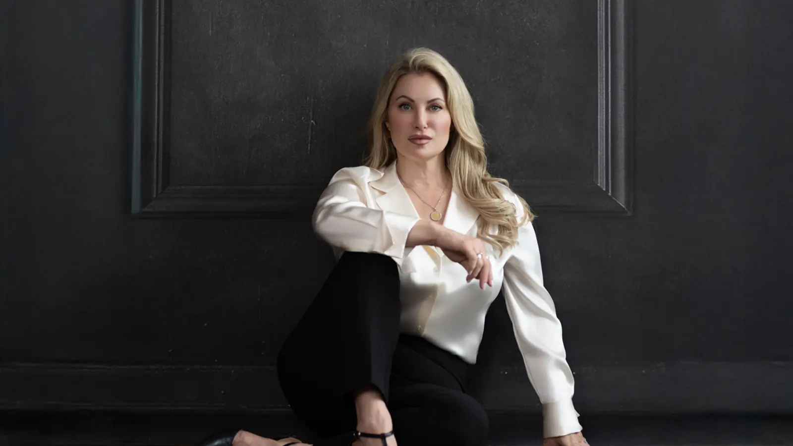 Woman in a solid ivory blouse photographed against a dark studio wall in Charlottesville